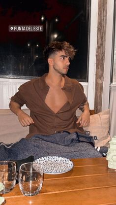 a man sitting on top of a wooden table next to a glass filled with wine