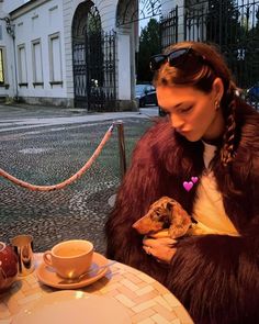 a woman sitting at a table with a dog in her lap and coffee cup next to her