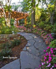 a stone path in the middle of a garden with pink flowers and trees around it