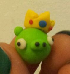 a green toy with a yellow crown on it's head sitting in someones hand