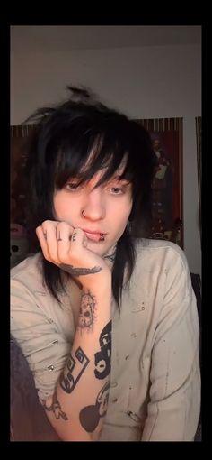 a woman with black hair and tattoos on her arm is posing for the camera while holding her hand up to her face