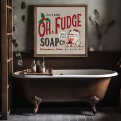 an old fashioned bathtub in a bathroom next to a framed sign that reads oh fudge soap co