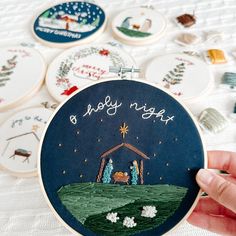 someone is holding up a hand embroidered christmas ornament in front of several other embroideryed ornaments