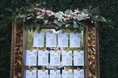 a wedding seating chart with flowers and greenery on the wall in front of it