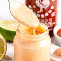 a spoon full of liquid being poured into a jar with limes in the background