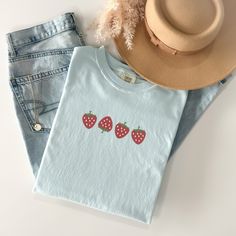 Welcome the sunny days with our delightful Summer Strawberry Embroidered T-Shirt! Made from 100% cotton, this t-shirt is not only comfortable but also perfect for staying cool during warm weather. Available in sizes S to 2XL and nine vibrant colors including Banana, Bay, Blossom, Butter, Chalky Mint, Chambray, Ivory, Orchid, and Peachy, there's a shade to suit every style.The standout feature of this t-shirt is the charming summer fruit-inspired design, showcasing four intricately embroidered strawberries on the center chest. Whether you're heading to a picnic, beach outing, or simply enjoying a leisurely day, this t-shirt adds a touch of sweetness to your summer wardrobe.Please note that colors may vary slightly due to monitor settings. For accurate sizing, refer to the size charts provid Casual Summer T-shirt With Embroidered Graphics, Trendy Embroidered Summer T-shirt, Trendy Summer T-shirt With Embroidered Text, Cute Organic Cotton T-shirt For Everyday, Trendy T-shirt With Embroidered Text For Summer, Casual Embroidered Graphic T-shirt For Summer, Summer Embroidered Graphic Tee, Cute Organic Cotton T-shirt For Spring, Blue Embroidered T-shirt For Summer