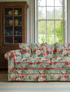 a floral couch sitting in front of a window next to a book shelf and cabinet