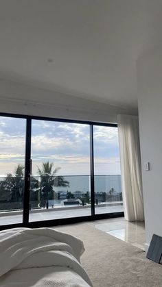 an empty bedroom with large windows overlooking the ocean and palm trees in front of it