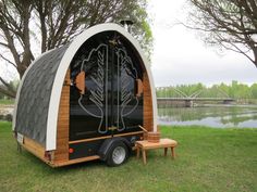 a small black and white trailer sitting on top of a lush green field next to a lake