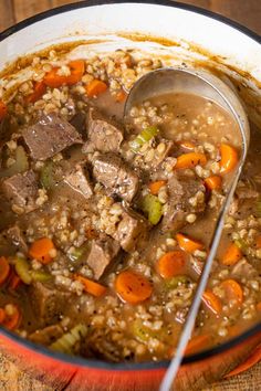 a bowl filled with meat and rice soup on top of a wooden table next to a spoon