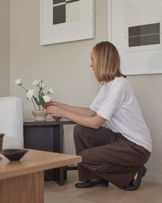 a woman kneeling down next to a vase with flowers in it on top of a table