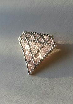 a small triangle shaped brooch sitting on top of a white table next to a wall