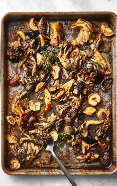 an overhead view of mushrooms and herbs on a baking sheet with a spoon in it