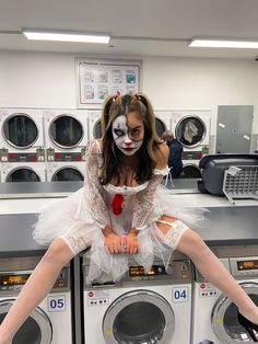 a woman dressed as a clown sitting on top of a stack of washers in a laundry room