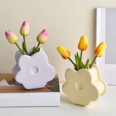 two vases with yellow and pink flowers in them next to a book on a table