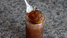 a spoon full of caramel sauce on top of a jar filled with something else