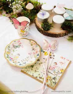 a table topped with plates and cupcakes on top of a white table cloth