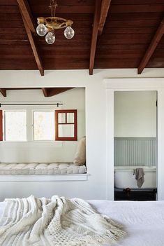 a white bed sitting under a window next to a wooden ceiling mounted light above it's headboard