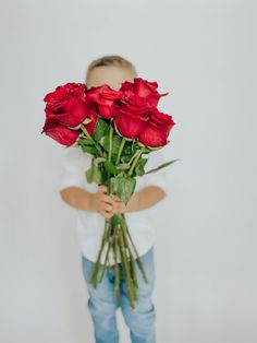 a young boy holding red roses in his hands