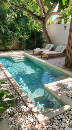 a small swimming pool surrounded by rocks and trees with lounge chairs around it in the background