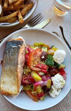 a white plate topped with fish and veggies next to french fries on a table