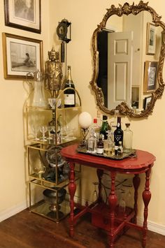 a red table topped with lots of bottles and glasses next to a wall mounted mirror