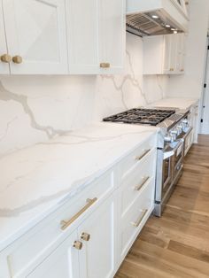 a kitchen with white cabinets and marble counter tops, an oven and stove top in the middle