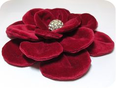 a red flower with a diamond brooch on it's center sits on a white surface