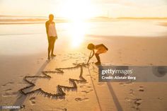 two people are writing on the sand with their hands and drawing in the sand at sunset