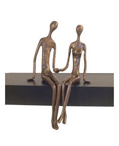 two bronze figurines sitting on top of a black book shelf with one holding the other's hand