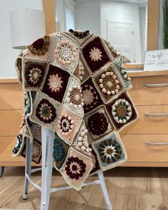 a crocheted blanket sitting on top of a chair in front of a dresser