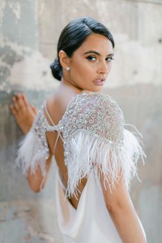 a woman in a white dress with feathers on her shoulders and back, looking at the camera