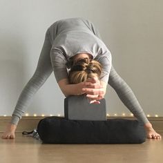 a woman is doing yoga on the floor with her hands behind her head and legs bent forward