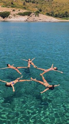 four people floating in the water with their arms around each other while doing acrobatic tricks