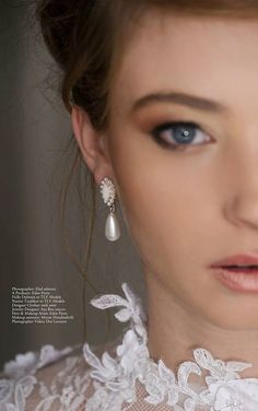 a woman with blue eyes and white lace on her neck is wearing earrings that have pearls hanging from them