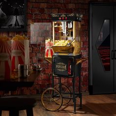 an old fashioned popcorn vending machine on wheels in front of a brick wall and wooden floor