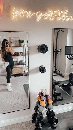 a woman taking a selfie in front of a mirror with dumbs and exercise equipment