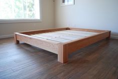 a wooden bed frame sitting on top of a hard wood floor next to a window