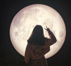 a woman is standing in front of the moon with her hand up to her face