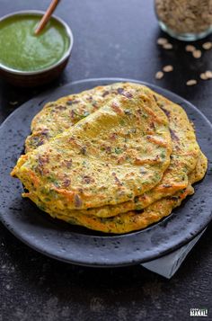 some food is on a black plate and there are two bowls with green sauce in the background