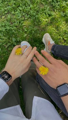 a person sitting in the grass with two yellow flowers on their fingers and an apple watch