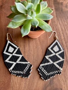 a pair of black and white beaded earrings next to a succulent plant