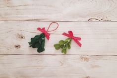 two green leaves with red bows are on a white wooden surface, one is tied in a bow