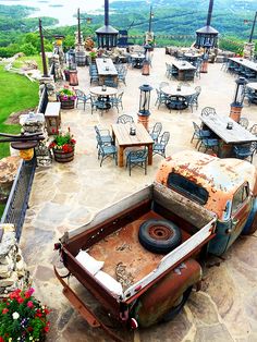 an old truck is sitting in the middle of a patio with tables and chairs around it