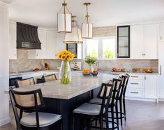 a large kitchen with white cabinets and marble counter tops, black bar stools, yellow flowers on the island