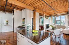 an open concept kitchen and living room with hardwood floors, white furniture and exposed ceilings