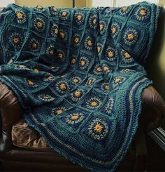 a blue crocheted blanket sitting on top of a brown leather chair next to a window