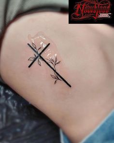 a small cross tattoo on the back of a woman's left shoulder, with two crossed swords sticking out of it