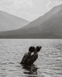 two people in the water kissing each other with mountains in the backgrouund