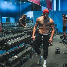 a man with no shirt is walking through a gym filled with dumbs and exercise equipment